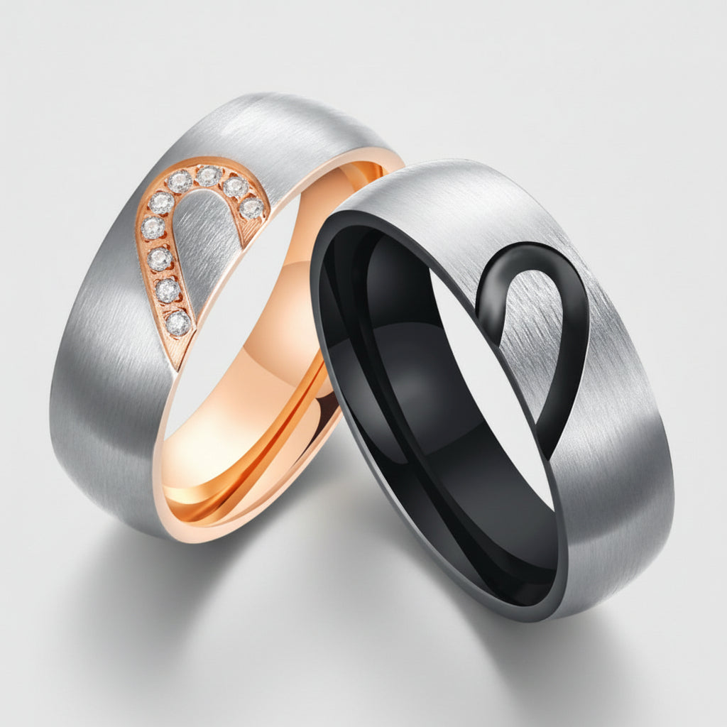 Two rings, one silver with rose gold heart design and the other black with silver heart design, on a white background.